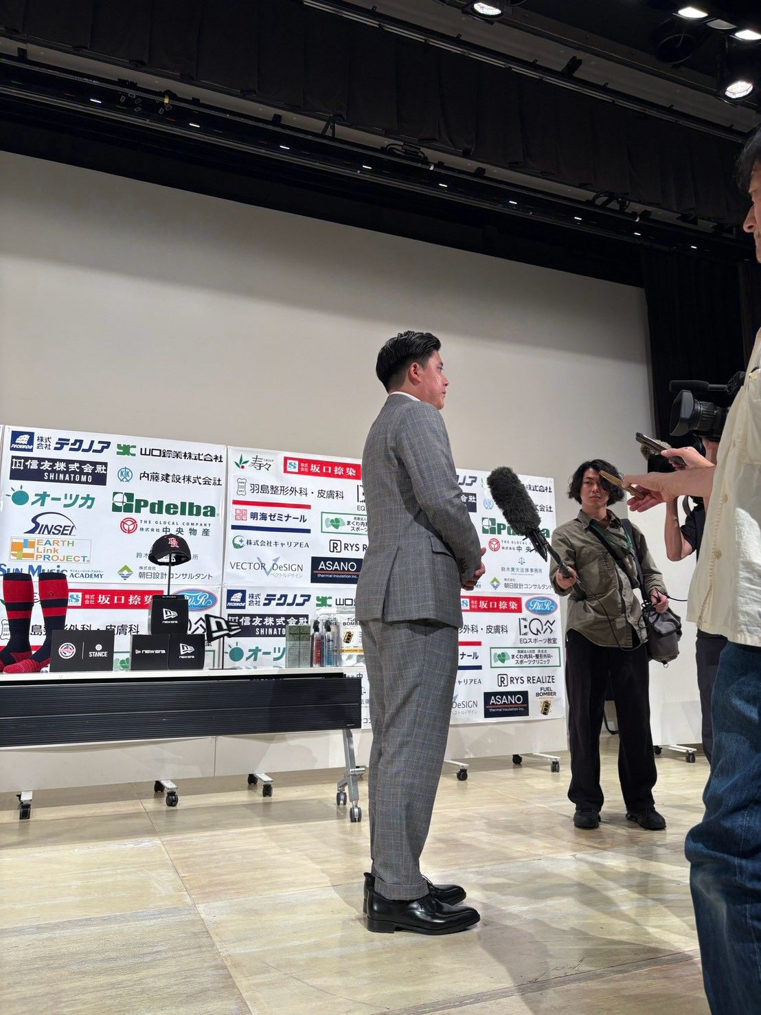 グレーのスーツ姿で報道陣の取材に応じる若松駿太監督