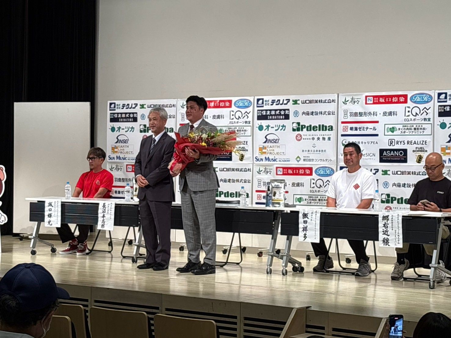 就任会見のステージで花束を受け取った若松駿太監督（右）と来賓