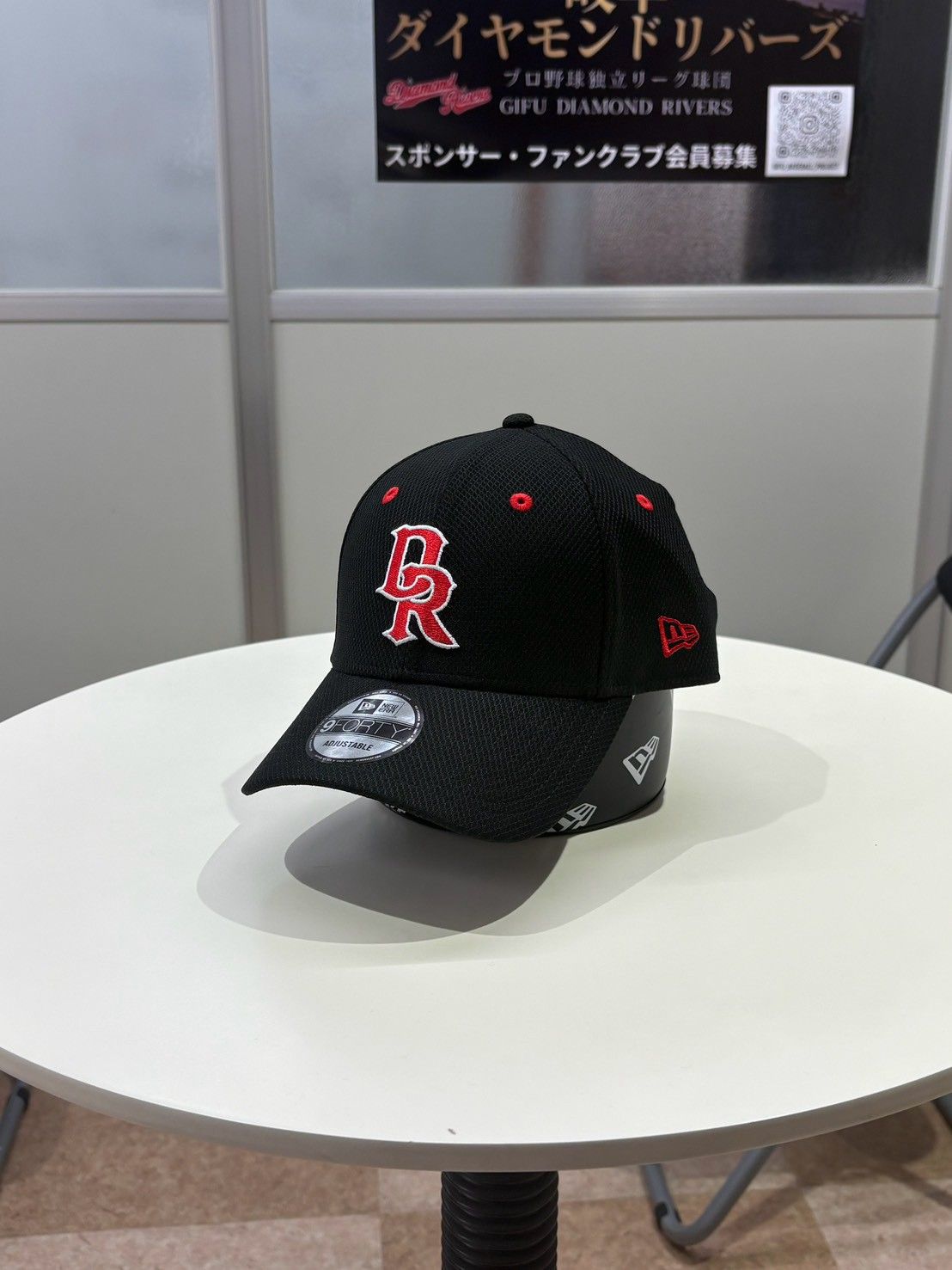 白いテーブルに置かれた、赤い「DR」の刺しゅう入りの黒いNEW ERAのキャップ