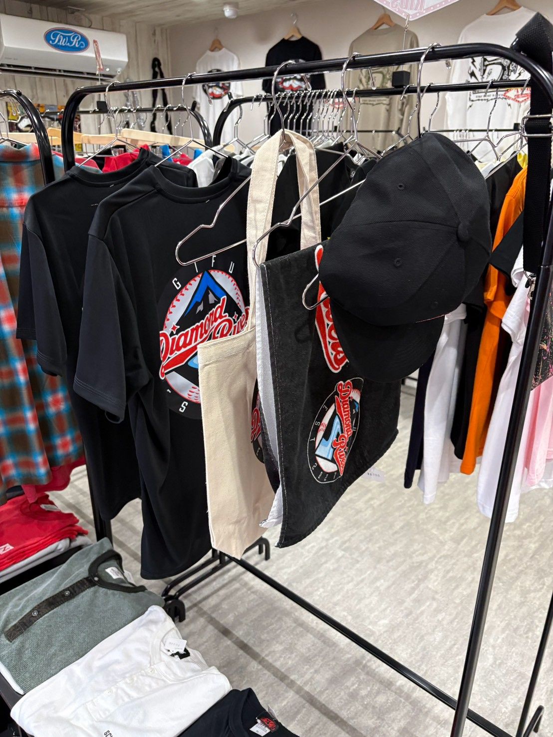 ハンガーラックに掛かった球団ロゴ入りのTシャツ、トートバッグ、キャップ